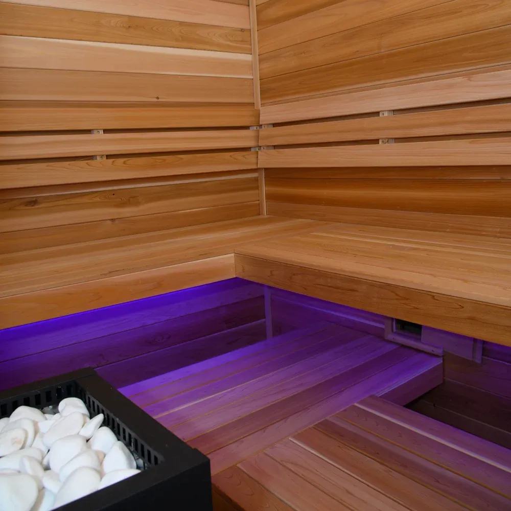 A timber sauna interior with tiered benches, a heater and under-bench lighting