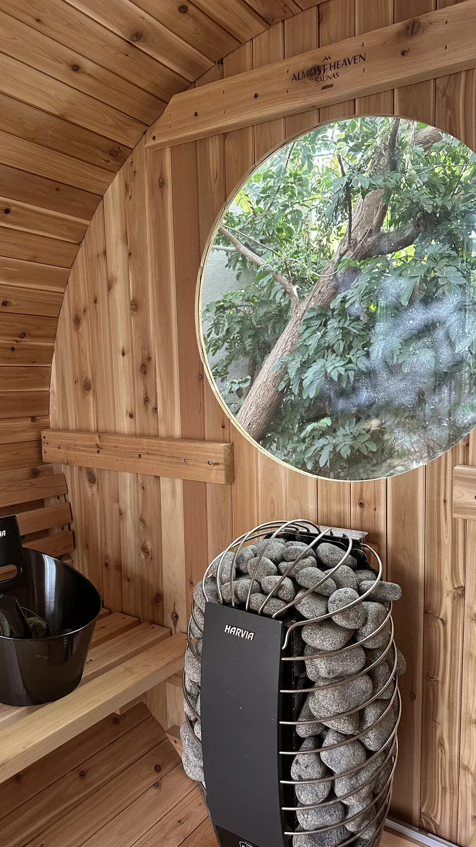 A stone-filled heater beside a circular window in a timber sauna